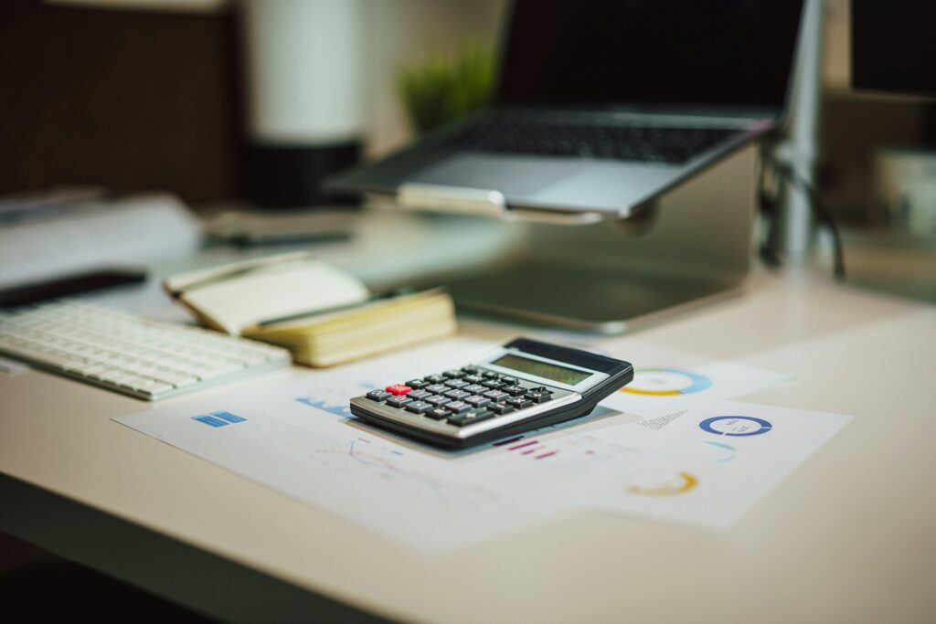 Calculator, charts, notebook, and laptop arranged on a desk.
