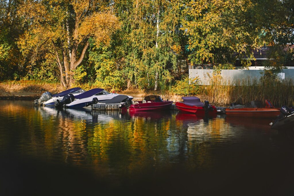 Small motorboats moored beside an autumn tree-lined shore.