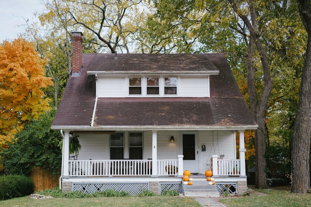 White house with a front porch framed by autumn trees.