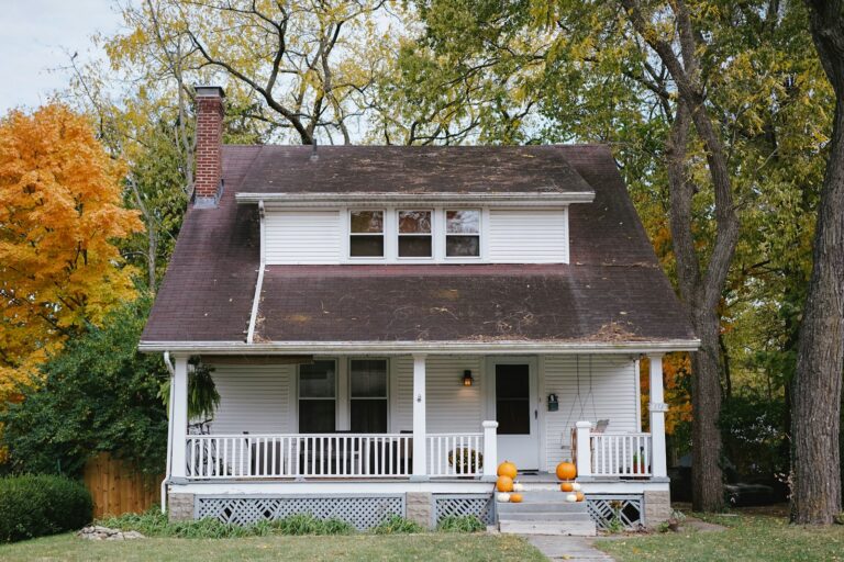 White house with a front porch framed by autumn trees.