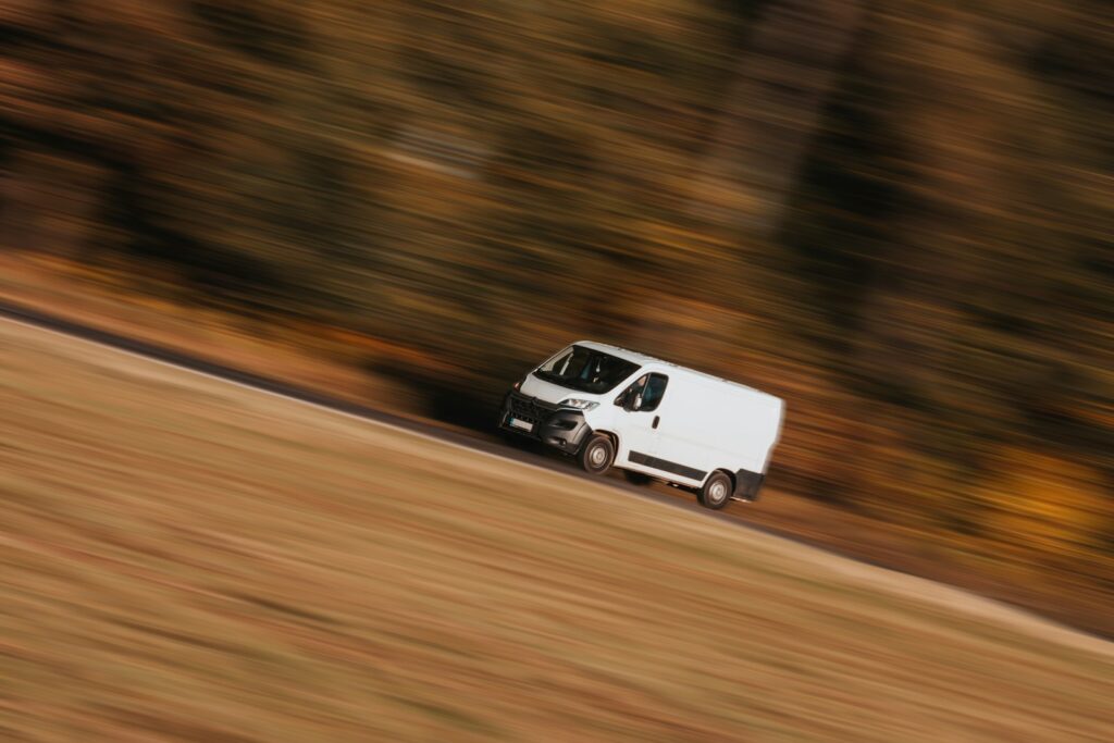 White cargo van traveling beside autumn trees.