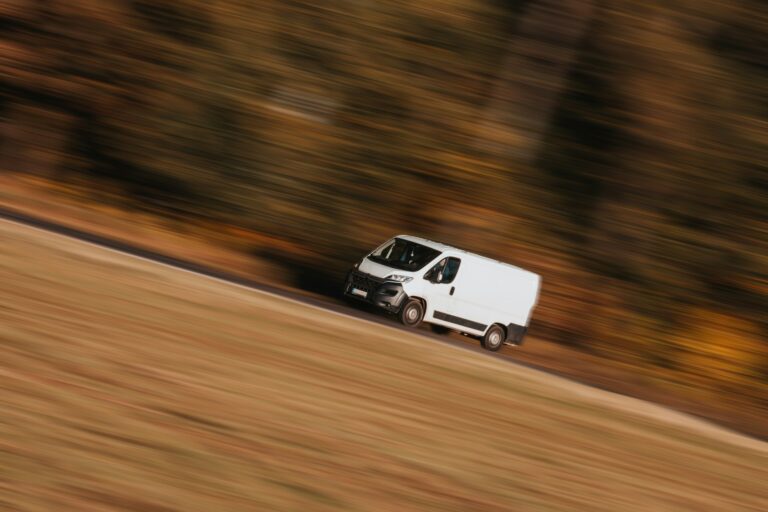 White cargo van traveling beside autumn trees.