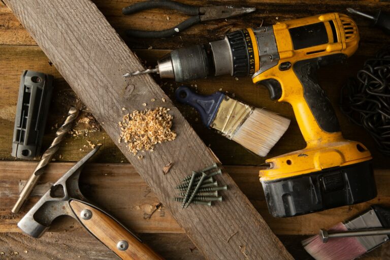 Cordless drill, hand tools, brush, and wood on a work surface.