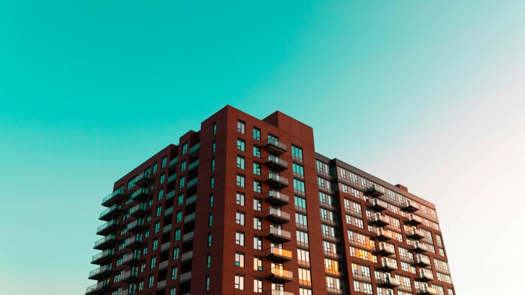 Brick apartment building with rows of balconies beneath a blue sky.