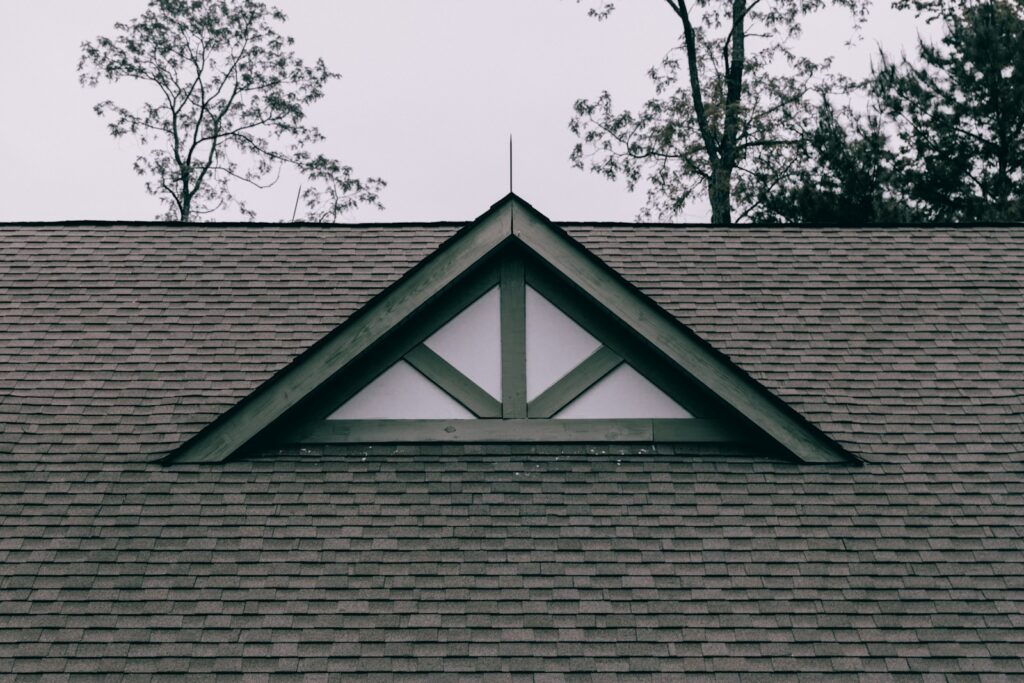 Shingled roof with a decorative gable and trees behind it.