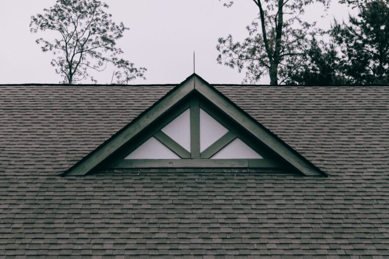 Shingled roof with a decorative gable and trees behind it.