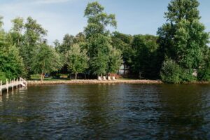 Tree-lined waterfront with a cabin, shoreline chairs, and a dock.